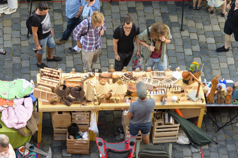 Blick aus der Vogelperspektive auf einen Verkaufsstand auf dem Trempelmarkt in Nürnberg. Auf dem Tisch befinden sich unzählige Gegenstände aus Holz. Ein Verkäufer steht hinter dem Tisch. Drei Besucher stehen vor dem Tisch und sehen sich die Waren an.