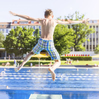Ein Junge springt im Westbad vom Sprungbrett ins Wasser.