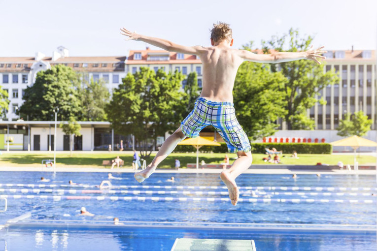 Ein Junge springt im Westbad von einem Sprungbrett ins Becken.