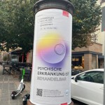 Man sieht eine Litfaßsäule, die mit einem Plakat für die Nürnberger Woche der seelischen Gesundheit beklebt ist. Auf dieser steht der Slogan: Psychische Erkrankung ist behandelbar.