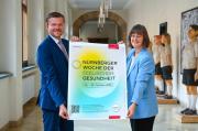 Oberbürgermeister Marcus König und Referentin für Umwelt und Gesundheit Britta Walthelm halten lächelnd das Plakat für die Nürnberger Woche der seelischen Gesundheit 2023 in die Kamera.