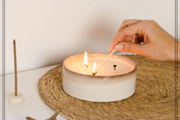 Ein Teelicht steht auf einer runden, kleinen Matte. Eine Hand ist zu sehen, die die Kerze mit einem Streichholz anzündet.Außenrum sind noch zwei Dekoelemente.