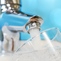 Wasser kommt aus einem silbernen Wasserhahn und fließt in ein Glas.