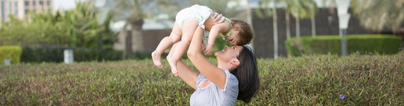 Eine Frau hält ein Baby in die Luft und lächelt es an.