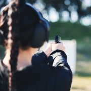 Eine Frau mit Zopf und Ohrenschutz schießt auf eine Zielscheibe.
