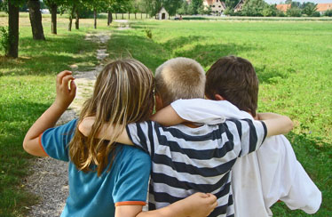 Drei Kinder, die Arm in Arm einen Weg entlang gehen.