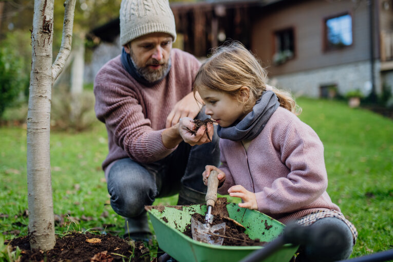 Little girl and father planting tree in garden in the spring, using compost. Girl smelling compost, learning abou composting. Concept of sustainable gardening family gardening.