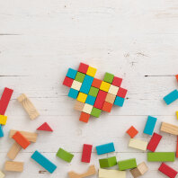 Top view of multi-colored wooden blocks scattered on a white wooden table. The cubes are stacked in the shape of a heart. School, education and training concept. Home games during self-isolation