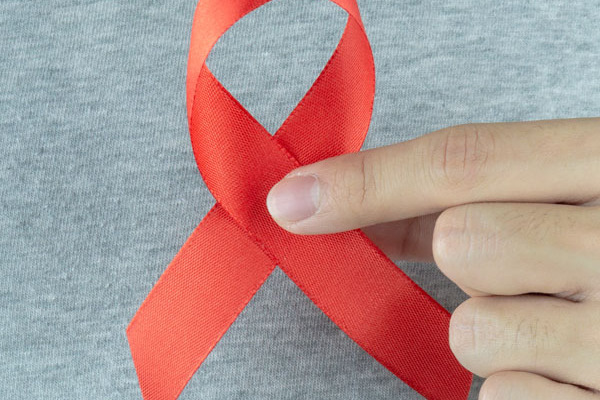 Eine Hand hält eine rote Aids-Schleife in die Kamera.