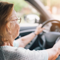 Eine ältere Frau sitz am Lenkrad eines fahrenden Autos.