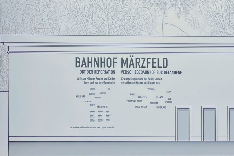 Entwurf der neuen Fassade des Bahnhofs Märzfeld als Erinnerungsort. Auf der Mauer, links oberhalb der zehn Türen, befindet sich ein Text mit Informationen.