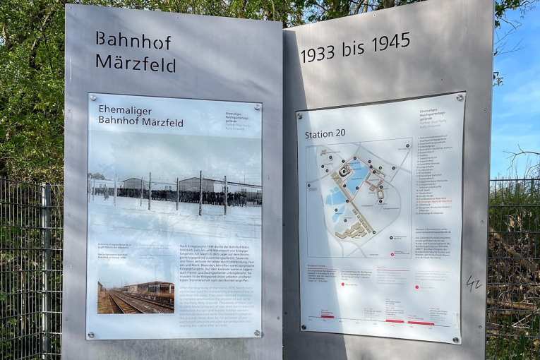Zwei Stelen informieren über die Geschichte des Bahnhofs Märzfeld in Nürnberg. Sie tragen die Überschriften "Ehemaliger Bahnhof Märzfeld" und "Station 20", enthalten Text und zeigen zwei Bilder und eine Grafik.