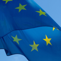 Eine Europa-Fahne weht im Wind. Ihre Grundfarbe ist blau. Darauf befindet sich ein Kreis mit gelben Sternen.