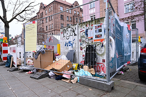 Kampagne gegen illegale Müllablagerung: Ein vermüllter Containerstandplatz ist mit Bauzäunen abgesperrt auf denen aufklärende Plakate angebracht sind. © Christine Dierenbach / Stadt Nürnberg