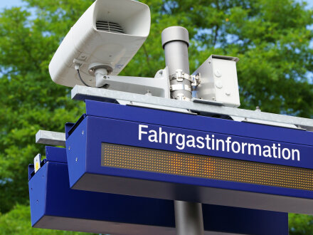 Das Bild zeigt einen Laut·sprecher an einem Bahn·steig. Darunter hängt eine Anzeige mit der Schrift: Fahrgastinformation.