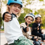 Kinder sitzen mit ihren Skateboards an einer Rampe.