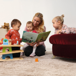Eine Tagesmutter sitzt auf dem Boden und liest drei Kindern ein Buch vor