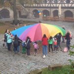 Auf dem Bild sind Kinder und Erwachsene zu sehen, die mit einem Balltuch spielen