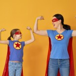 Eine Frau und ein Mädchen, die beide als Superheldin verkleidet sind und ihren Bizeps zeigen.