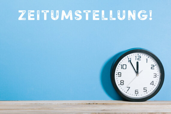 Foto von einer Wand·uhr am Boden. Über der Uhr steht das Wort: Zeit·umstellung.