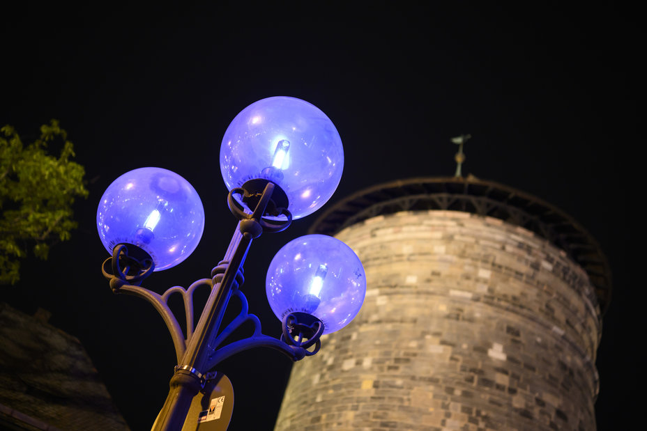 Vor einem Turm ist eine Straßenlaterne mit drei blau gefärbten Lampenschirmen gegen den Himmel zu sehen., Bild © (c) Steffen Kirschner l viaframe / Steffen Kirschner | viaframe