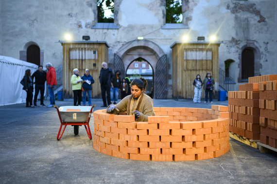 Die Künstlerin Sana Obaid mauert sich selbst in einem Turm aus roten Ziegelsteinen ein.