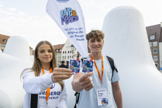 Ein Verkaufsteam aus einer jungen Frau und einem jungen Mann präsentiert den Blaue-Nacht-Pin, mit dessen Kauf Spenden gesammelt werden.