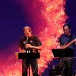 Vor einer Sonnenprojektion spielen ein Saxophonist und ein Gittarist.