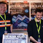 Zwei junge Männer verkaufen Tickets in einem Infokiosk.
