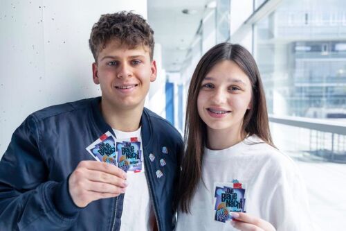 A young man and a young woman are holding the “Love & Peace” pins in their hands and wearing the badges on their jackets. © Nürnberger Versicherung