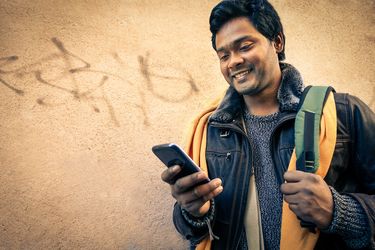 Young indian man holding mobile phone - Cheerful asian model next to old urban wall - Handsome businessman using connected smartphone outdoor