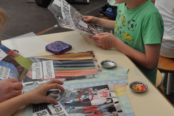 Kinder betrachten verschiedene Papiere mit Informationen zu Textilien, Firmen und Konsum.