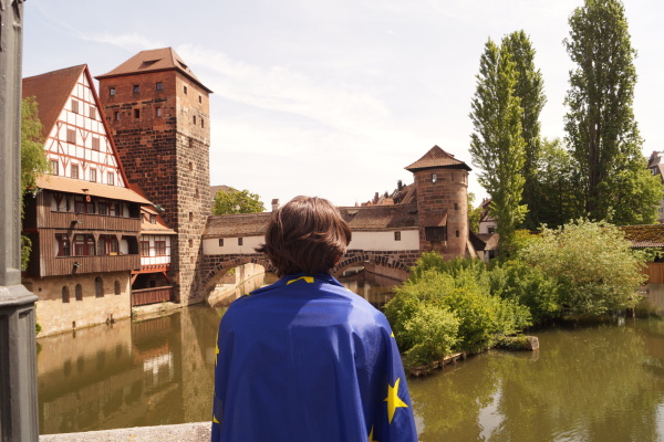 Eine Person, die eine Europaflagge umhängen hat, schaut auf die Pegnitz in der Nürnberger Altstadt.