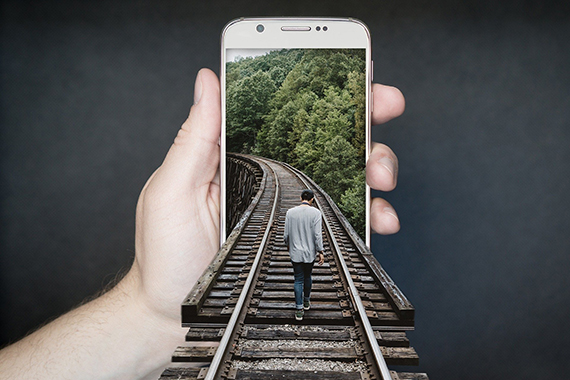 Mann läuft über Eisenbahnschienen vor Handy