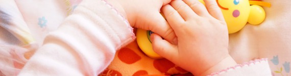 Das Bild zeigt Babyhände mit einem Spielzeug.