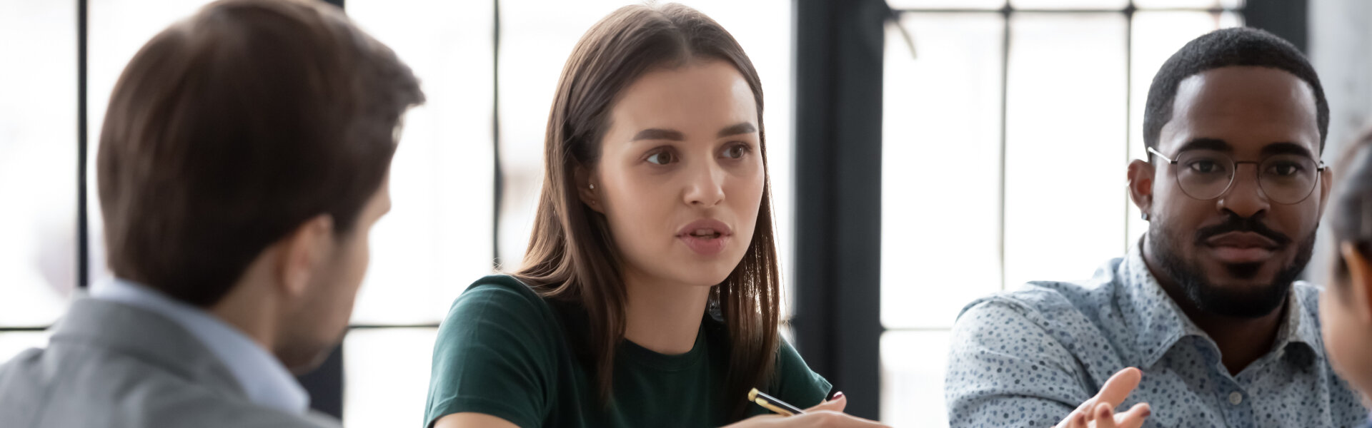 Two diverse multiethnic groups of business partners sitting at negotiation table, concentrated millennial female employee explaining plan project details to interested teammates on meeting in office
