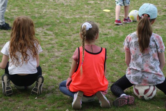 Drei Mädchen sitzen am Spielfeldrand auf den Fußbällen