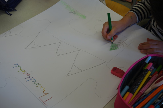 Ein Kind malt ein Plakat zum Thema Frieden mit der Umwelt. Es sind Bäume und Berge zu sehen.