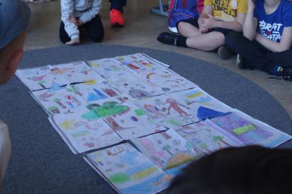 Die Kinder sitzen im Kreis auf dem Boden. In der Mitte liegt die aus vielen Teilen zusammen gesetze Vorlage für das große Kunstwerk.