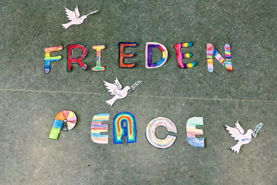Bunt bemalte Buchstaben, die die Wörter Peace und Frieden ergeben.