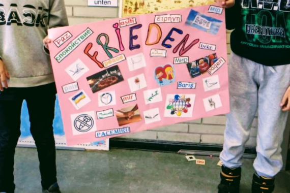 Die Schulkinder präsentieren ein Plakat zum Thema Frieden mit bunten Buchstaben und vielen Fotos.