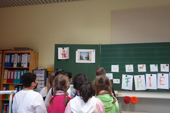 Die Kinder stehen vor der Tafel im Klassenzimmer und wählen ein Bild aus, das den Frieden für die darstellt