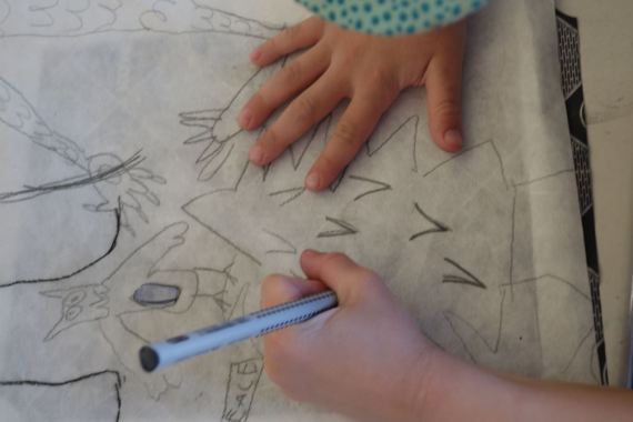 Ein Kind überträgt die Vorlage mit Kohlepapier auf das bunte Hanjipapier.