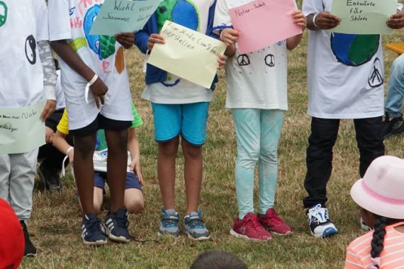 Kinder in selbst bemalten Tshirts halten Plakate zum Thema Frieden mit der Umwelt nach oben.