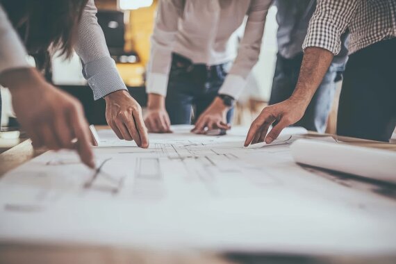 As architects and designers work on a creative project in an office setting, they discuss blueprints and brainstorm creative concepts.