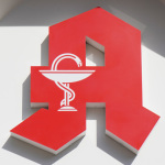 Rotes Apothekenlogo auf einer weißen Hauswand.