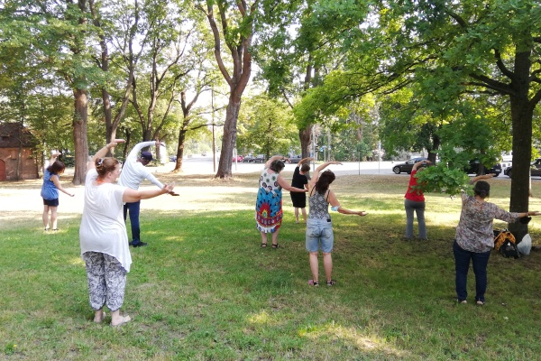 Mehrere Menschen stehen im Park und machen Dehnübungen.