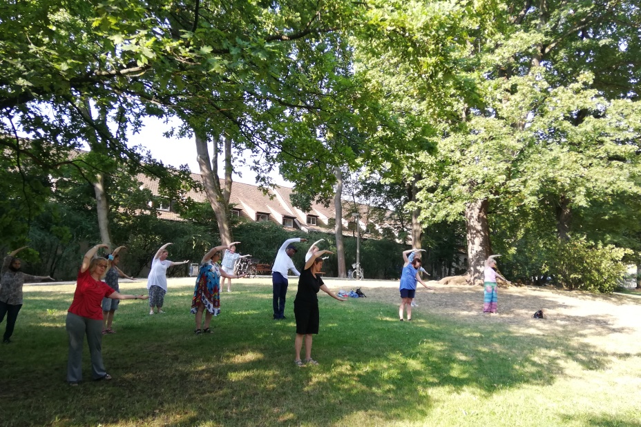 Menschen stehen in einem Park im Schatten von Bäumen und machen Dehnübungen., Bild © Stadt Nürnberg
