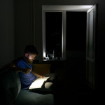 Ein Mann liest in einer Wohnung bei völliger Dunkelheit mit einer Taschenlampe ein Buch.