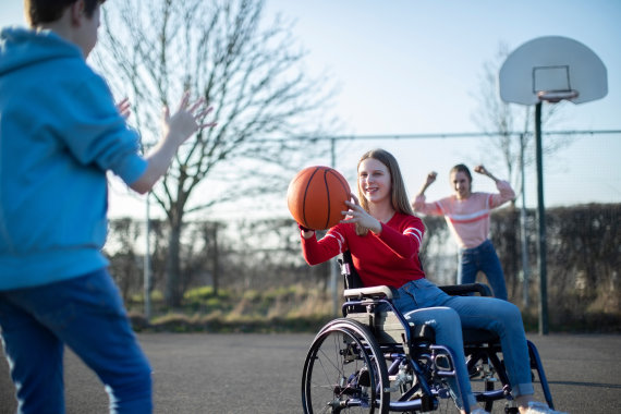 Teenage Girl In Wheelchair Playing Basketball With Friends
